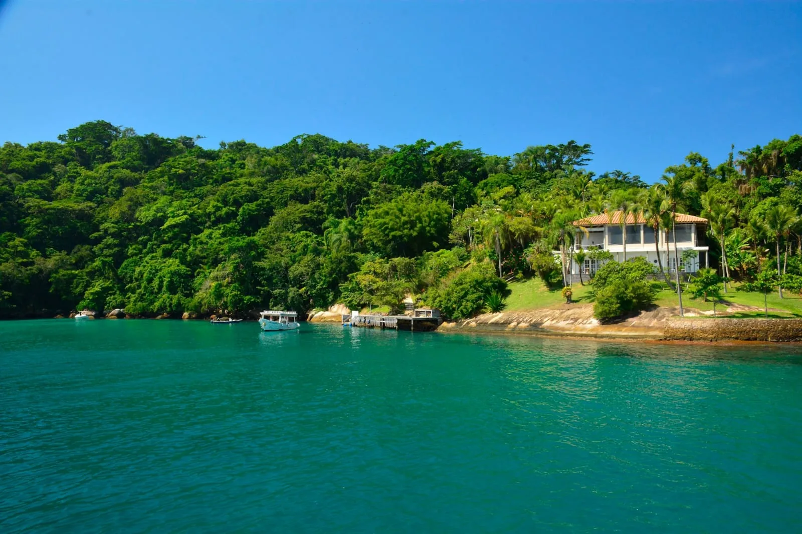 Píer e casa numa ilha da baía de Paraty, com barcos ancorados